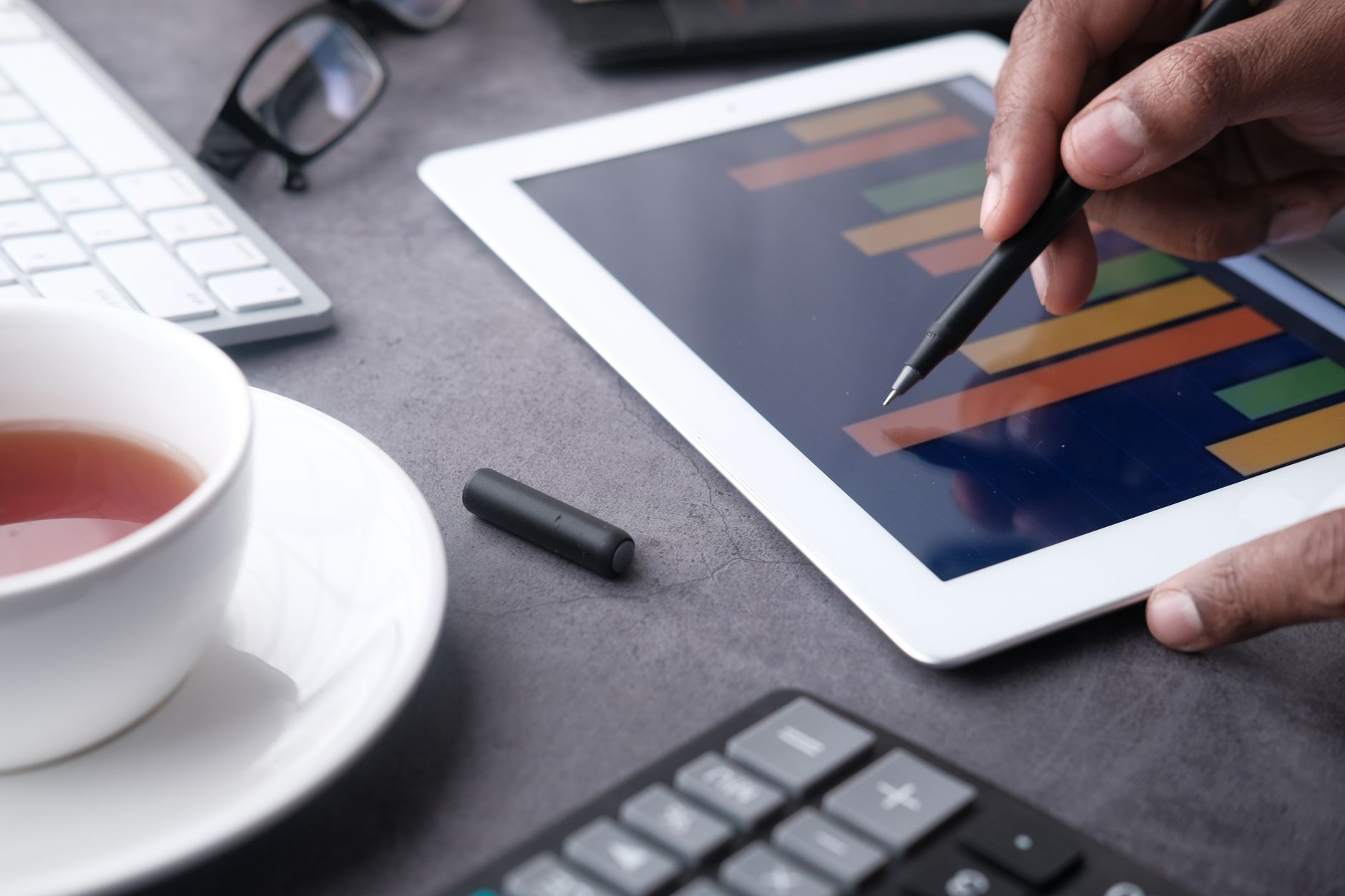 Hand using a stylus on a tablet displaying bar charts