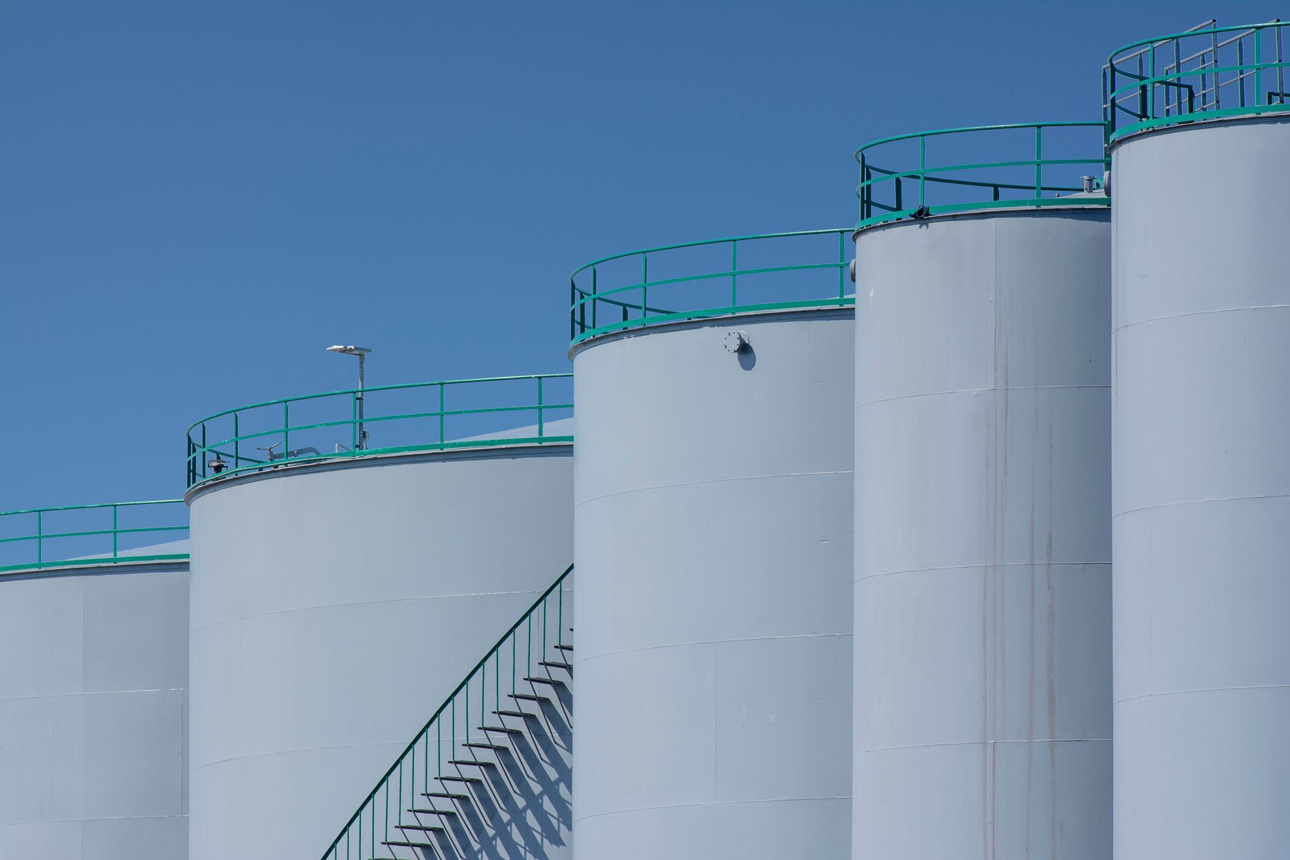 Large industrial storage tanks with green railings under a blue sky