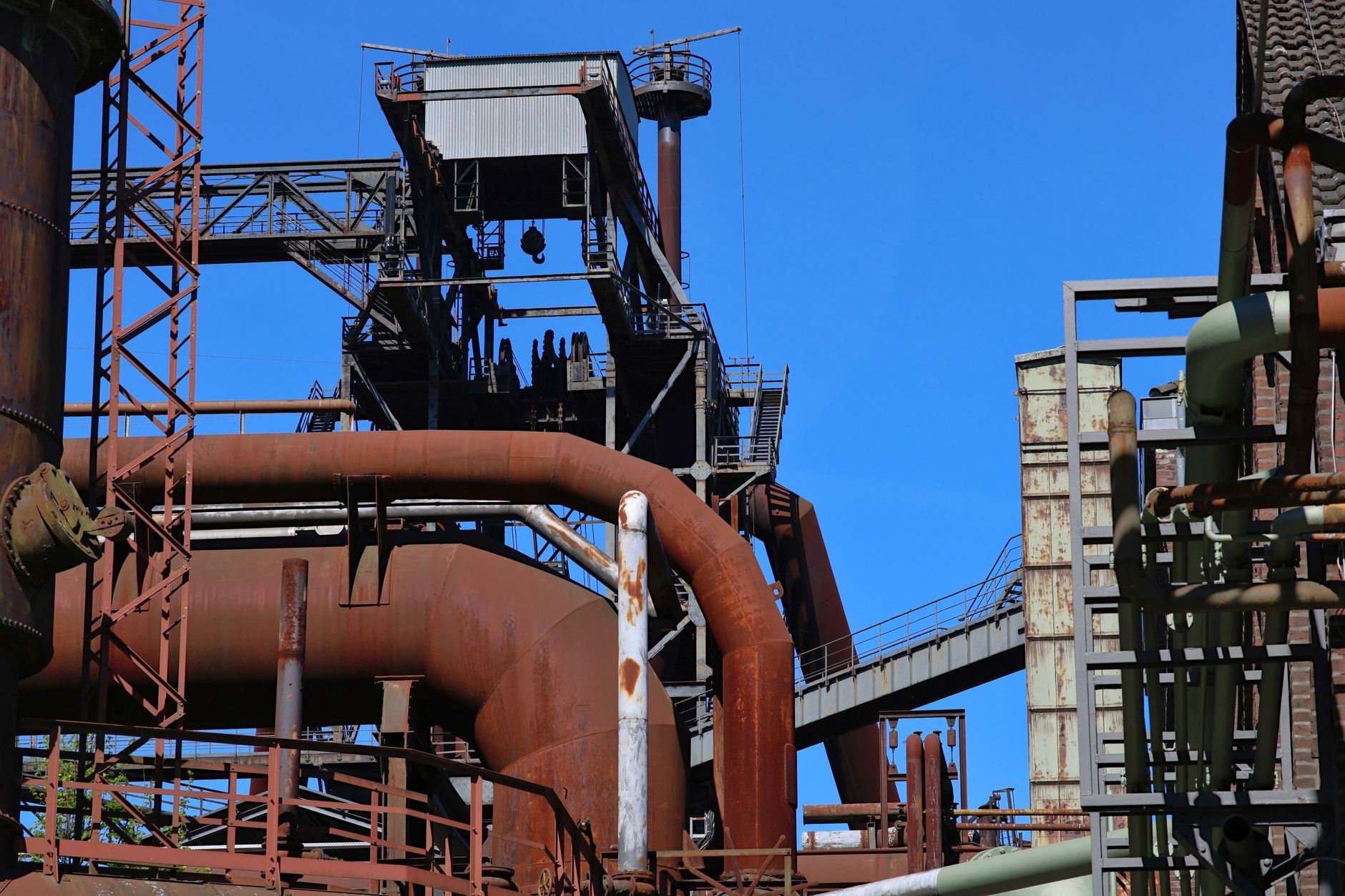 Rostige Rohre und Stahlkonstruktionen eines Hüttenwerks vor blauem Himmel